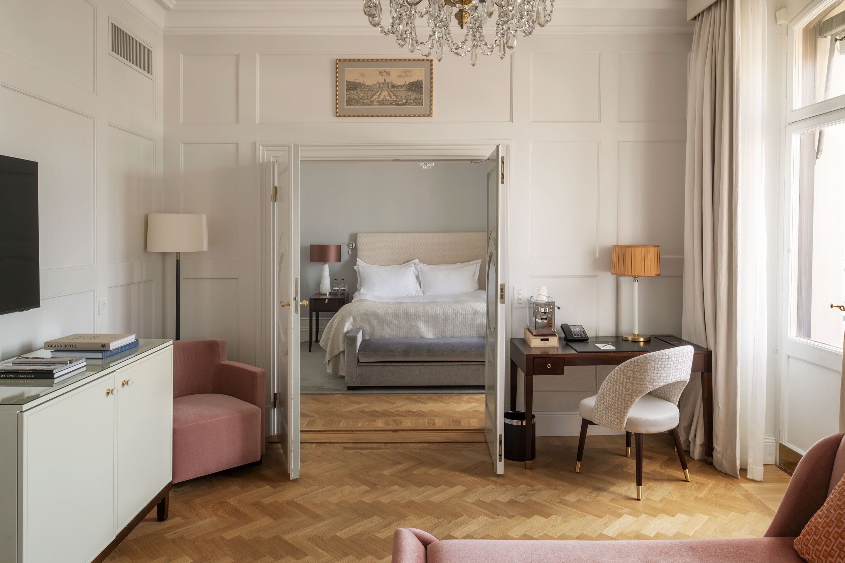 A hotel room with a bed, a desk with a lamp, a chair, a television, and a wardrobe.