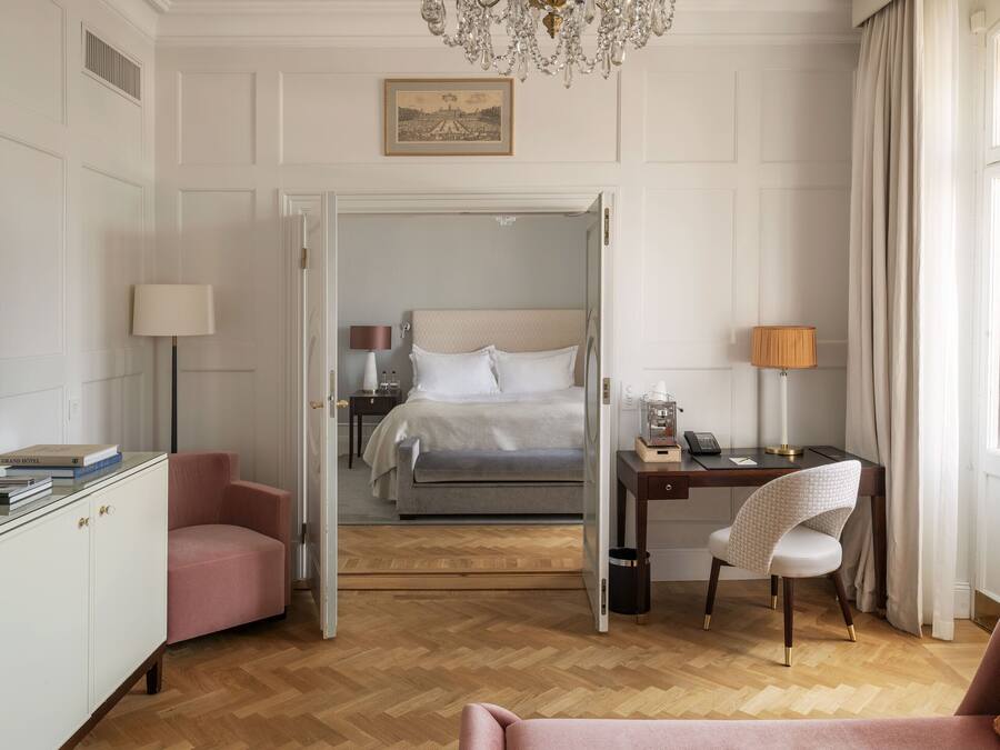 A hotel room with a bed, a desk with a lamp, a chair, a television, and a wardrobe.