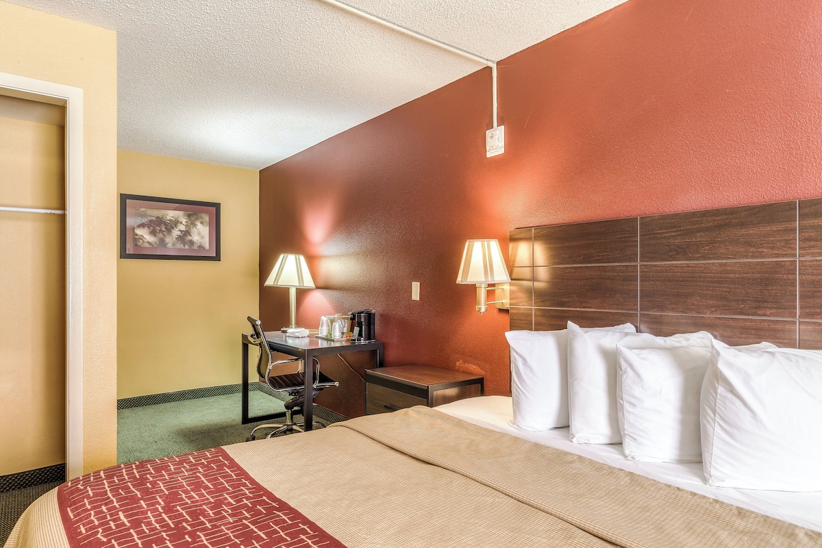 A hotel room with a bed, desk, chair, lamps, and a framed picture on the wall.