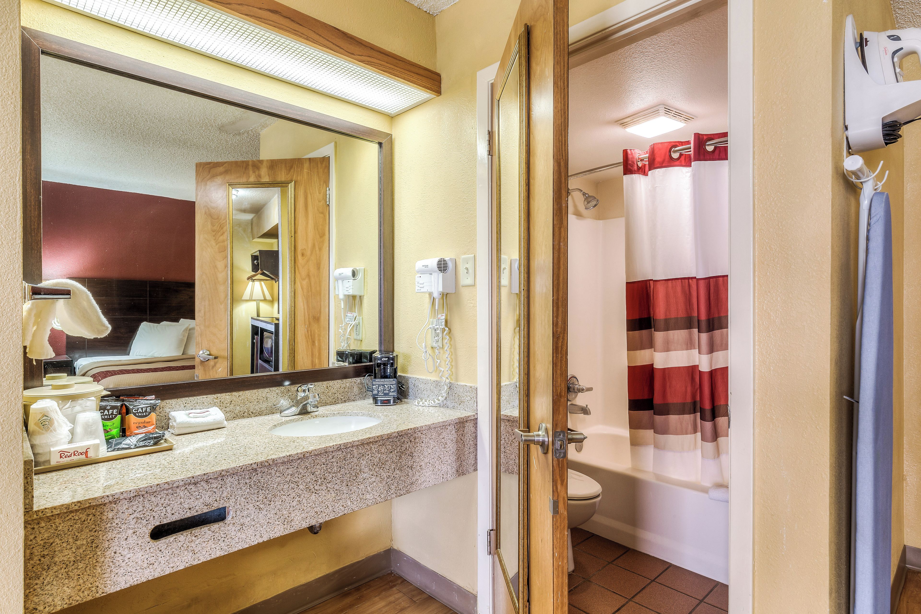Un baño de hotel con lavamanos doble, espejo, ducha e inodoro.