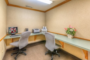 A corner office with two chairs, a desk, a printer, a computer monitor, and a vase with flowers.