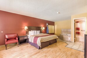 Une chambre d’hôtel comprenant un lit, une table de chevet, une lampe, ainsi qu’une salle de bain avec une baignoire et une douche.