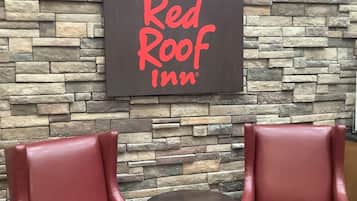 A Red Roof Inn sign on a stone wall with two red leather chairs and a small table.