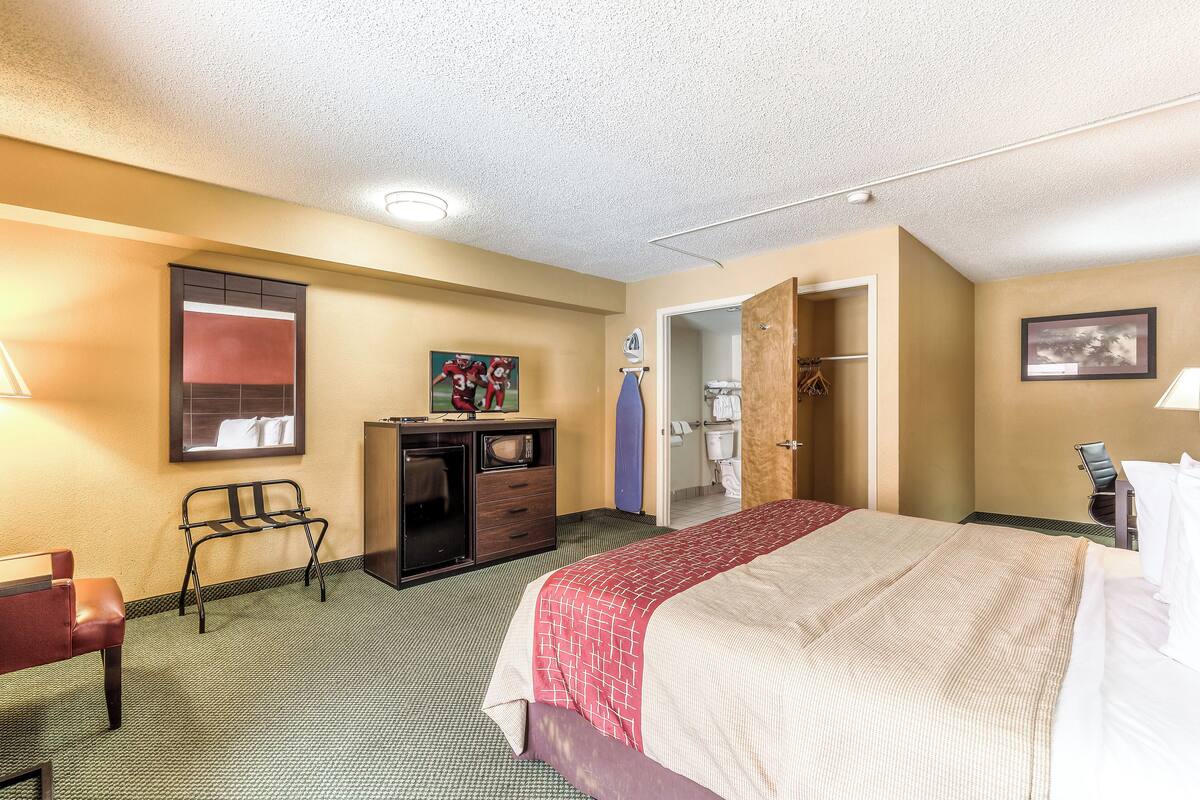 A hotel room with a bed, a desk, a chair, a wardrobe, and a bathroom visible through an open door.