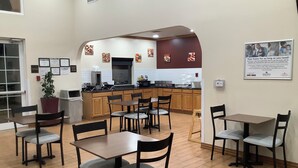 A dining area with tables and chairs, a kitchen in the background, and a sign on the wall. - Red Roof Inn Amarillo West (Amarillo)