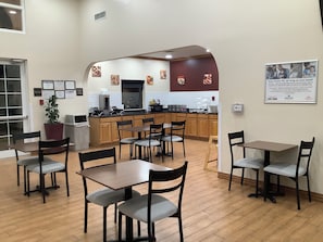 A dining area with tables and chairs, a kitchen in the background, and a sign on the wall. - Red Roof Inn Amarillo West (Amarillo)
