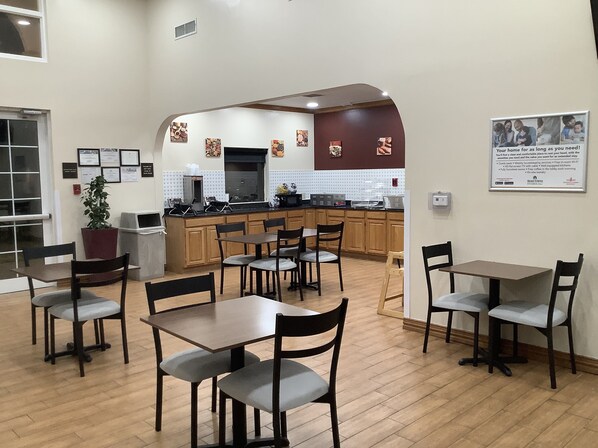 A dining area with wooden tables and chairs, a kitchen in the background, and a sign on the wall. - Red Roof Inn Amarillo West (Amarillo)