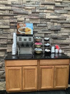 A coffee station with a coffee machine, a sign for iced coffee, and multiple bowls of food.