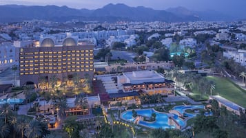 A hotel with a large building, a swimming pool, and a landscaped area with palm trees.