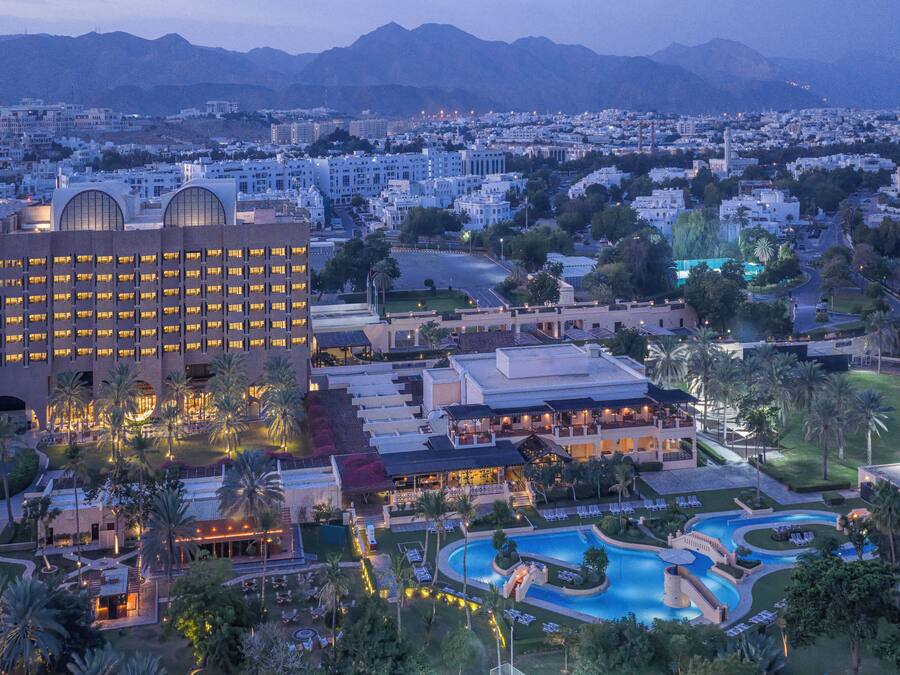 A hotel with a large building, a swimming pool, and a landscaped area with palm trees.