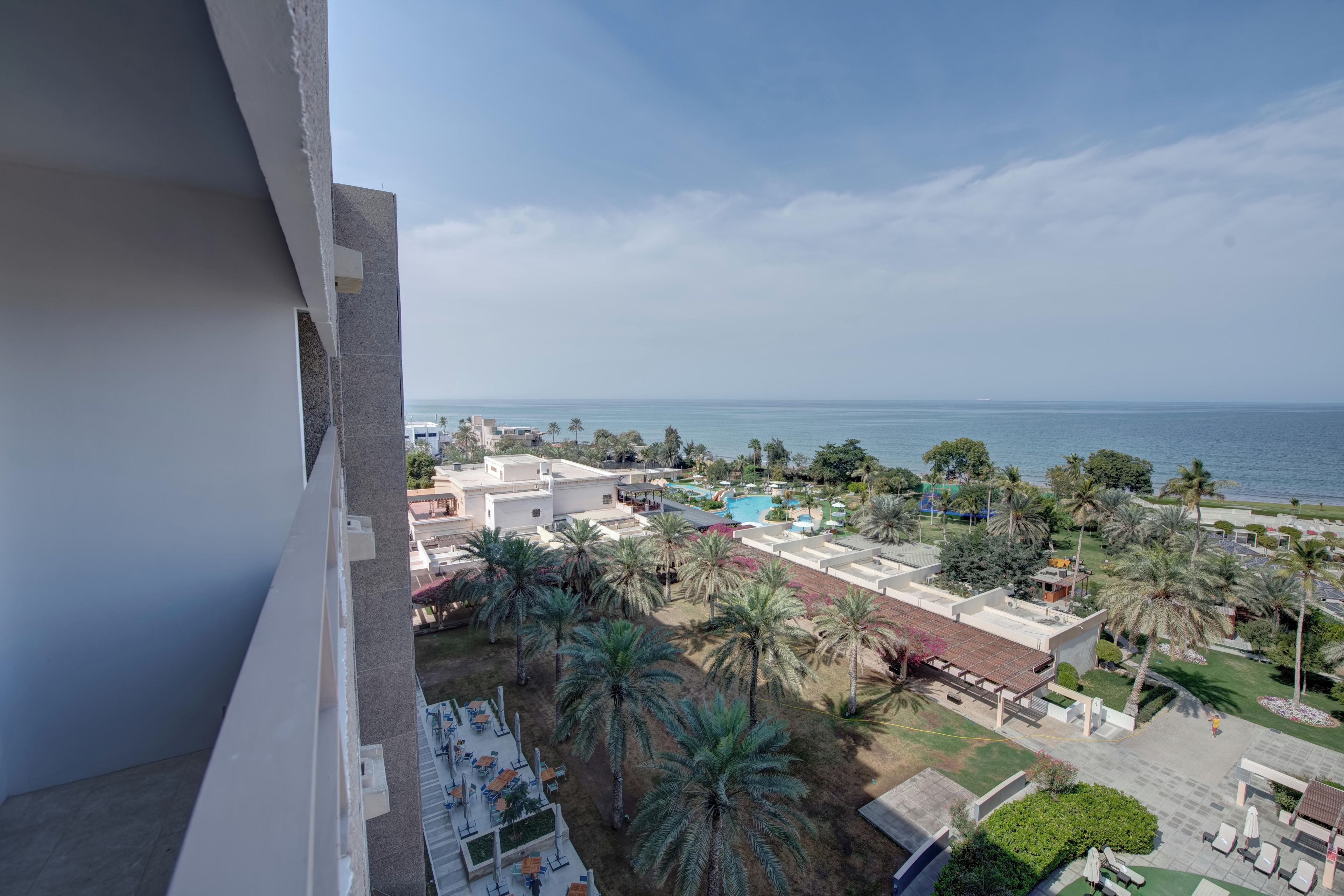 A resort with a pool, palm trees, and a view of the sea.