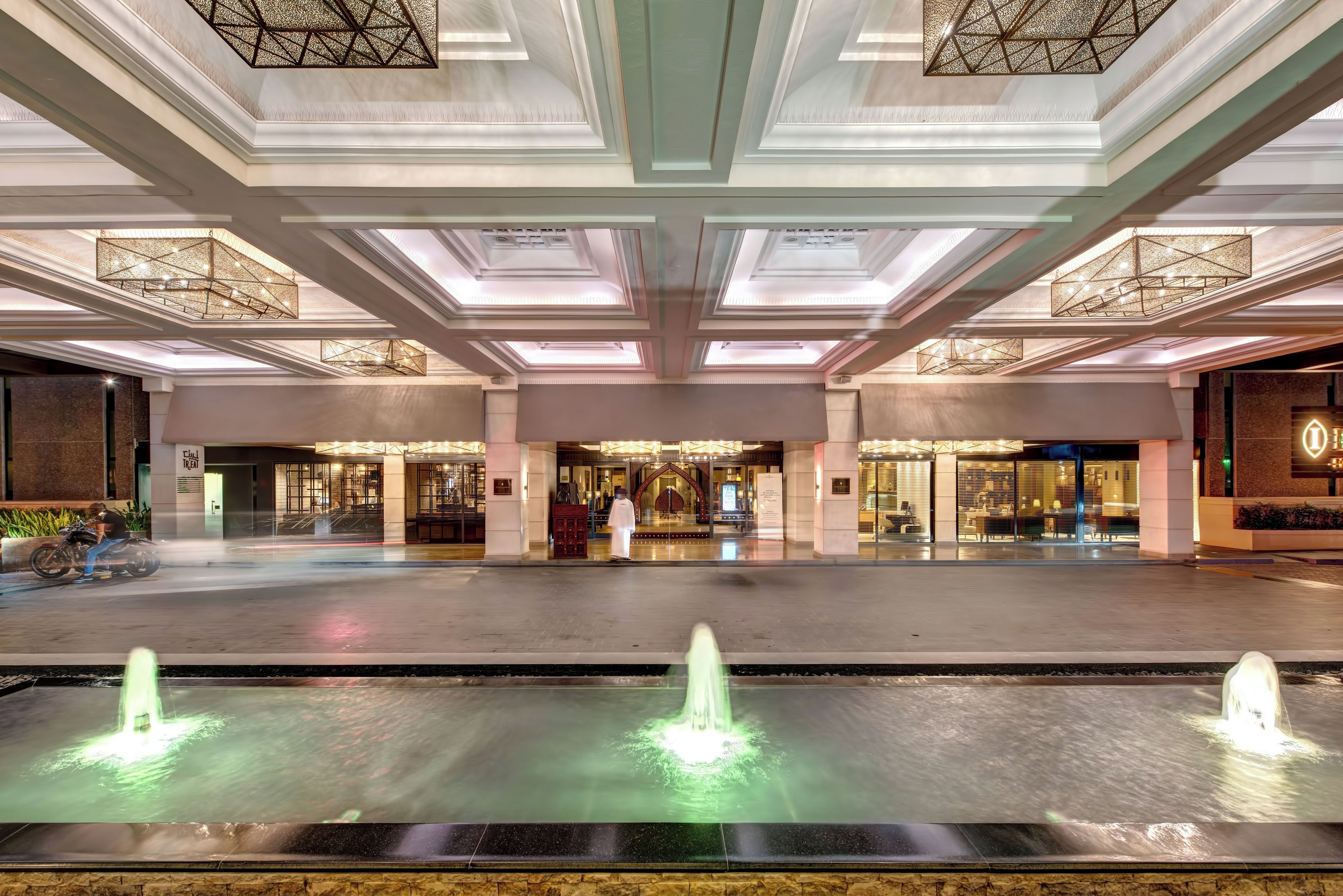 A spacious lobby with a central fountain, a grand staircase, and a modern ceiling design.