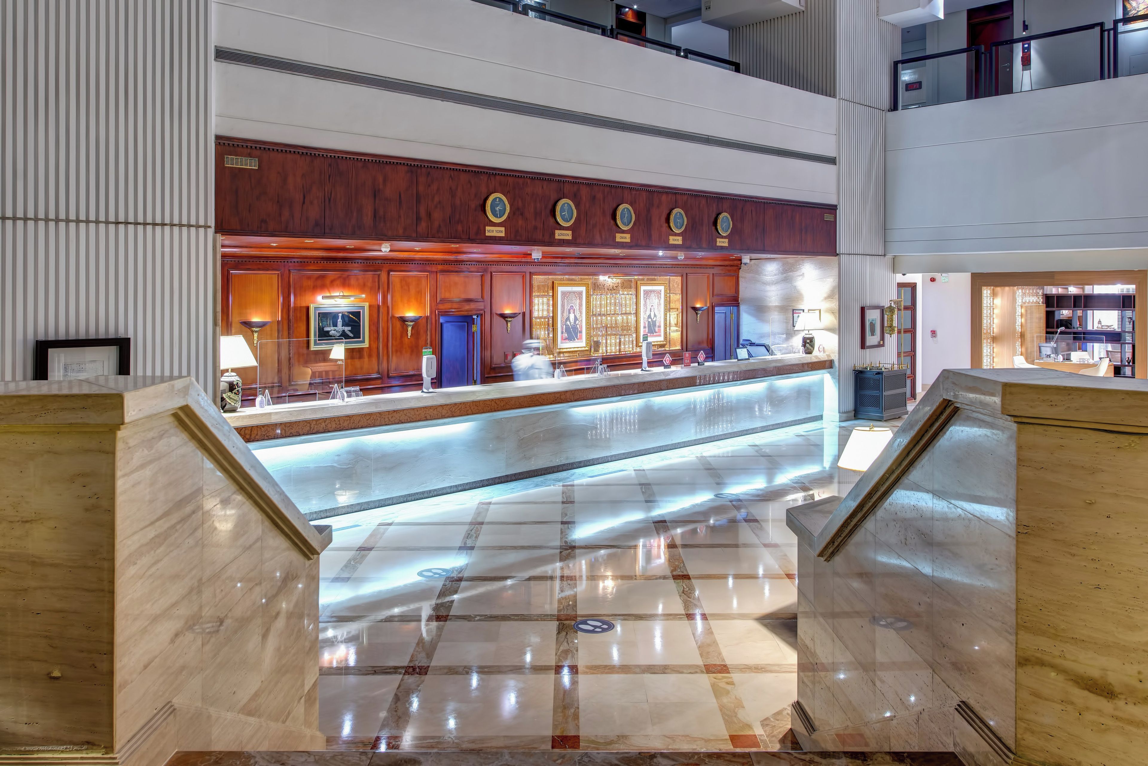 Un hall d’hôtel comprenant un comptoir d’accueil, un guichet d’enregistrement et un escalier menant à un étage supérieur.