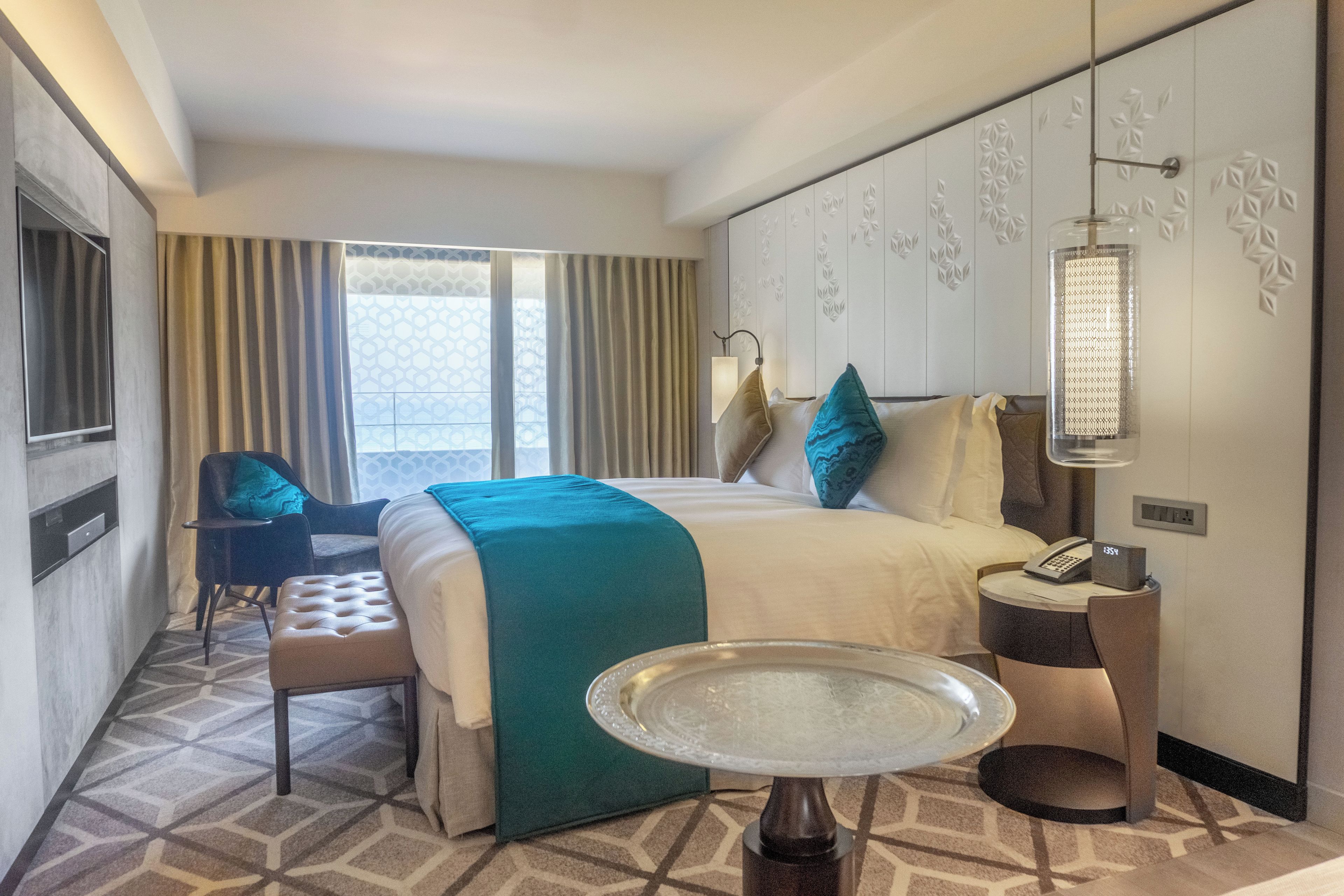 Habitación de hotel con cama, una silla, una mesita y teléfono en la pared.
