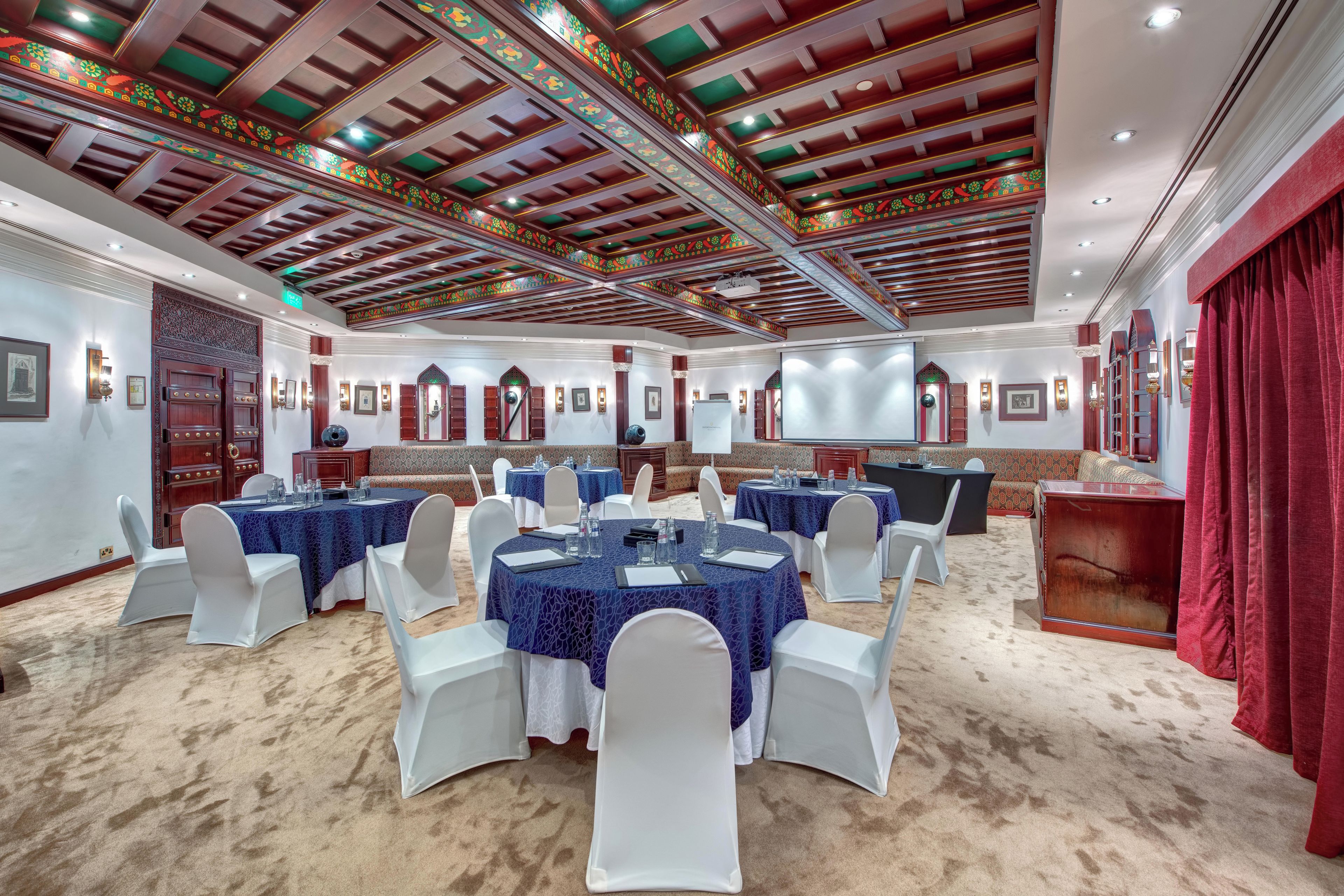 Un salón de conferencias con mesas redondas, sillas blancas y una cortina roja.
