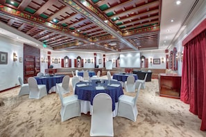 Un salón de conferencias con mesas redondas, sillas blancas y una cortina roja.
