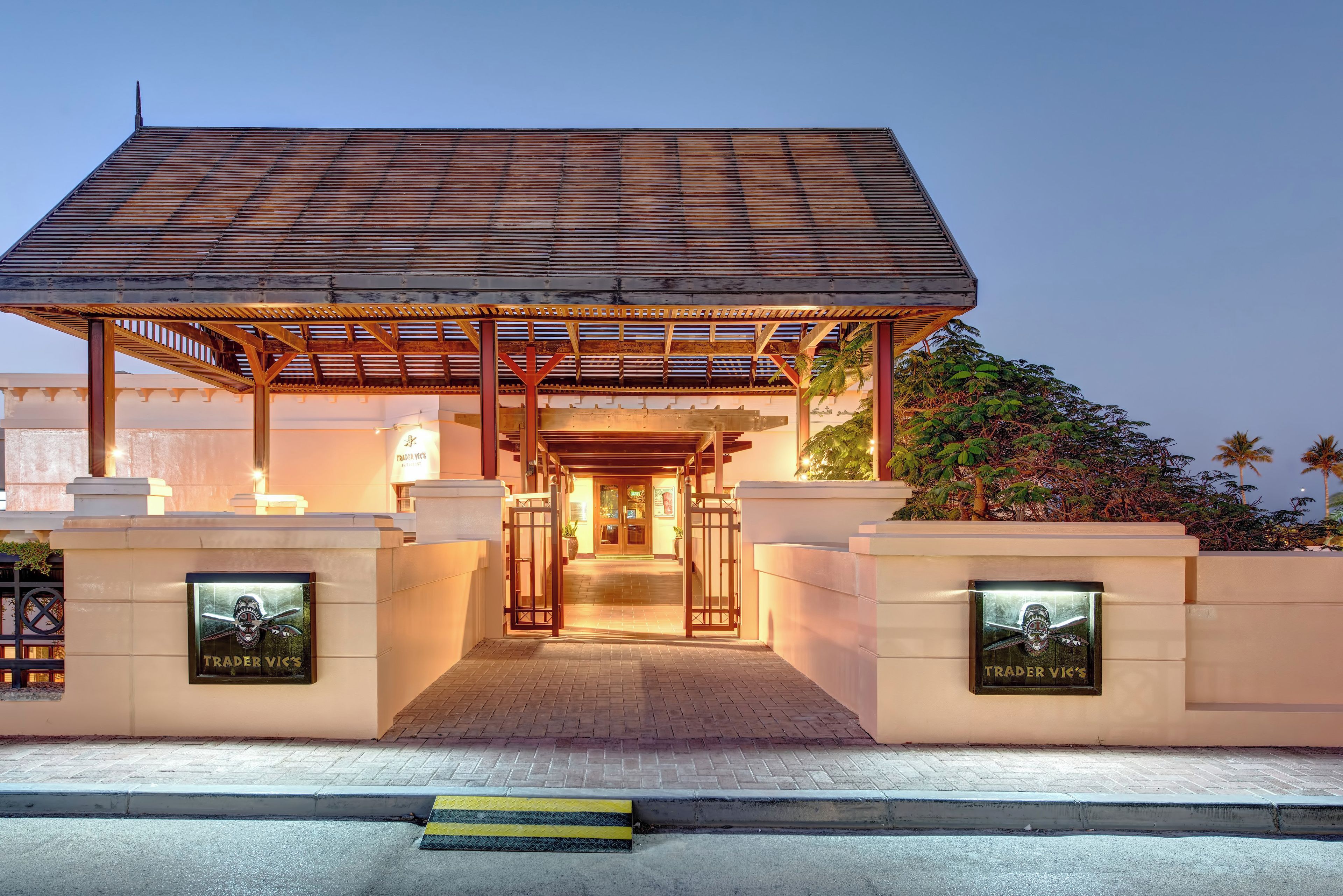 Entrada de hotel con una galería techada, acceso mediante portón y dos letreros que dicen 'TRADER VIC'S'.