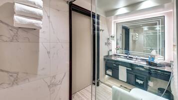A modern bathroom with a glass shower enclosure, a marble-tiled wall, and a vanity with a large mirror.