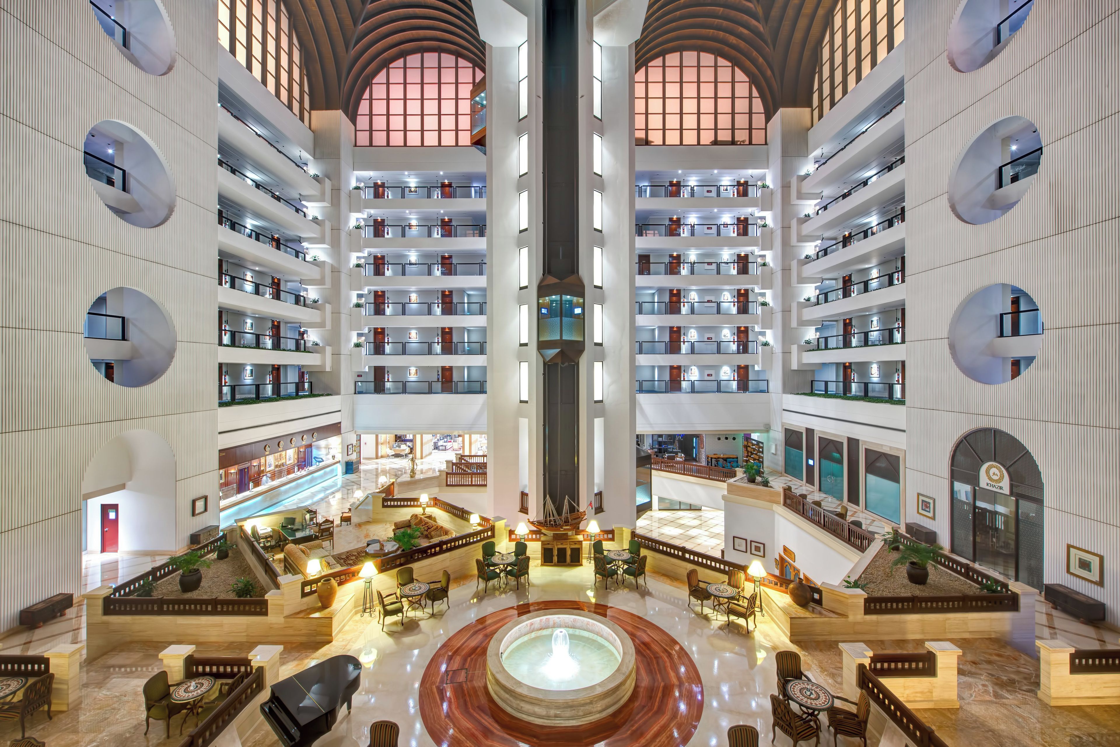 A multi-level hotel lobby with a central atrium, multiple floors with balconies, and a fountain in the middle.