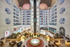 Vestíbulo de hotel de varios niveles con un atrio central, múltiples pisos con balcones y una fuente en el centro.