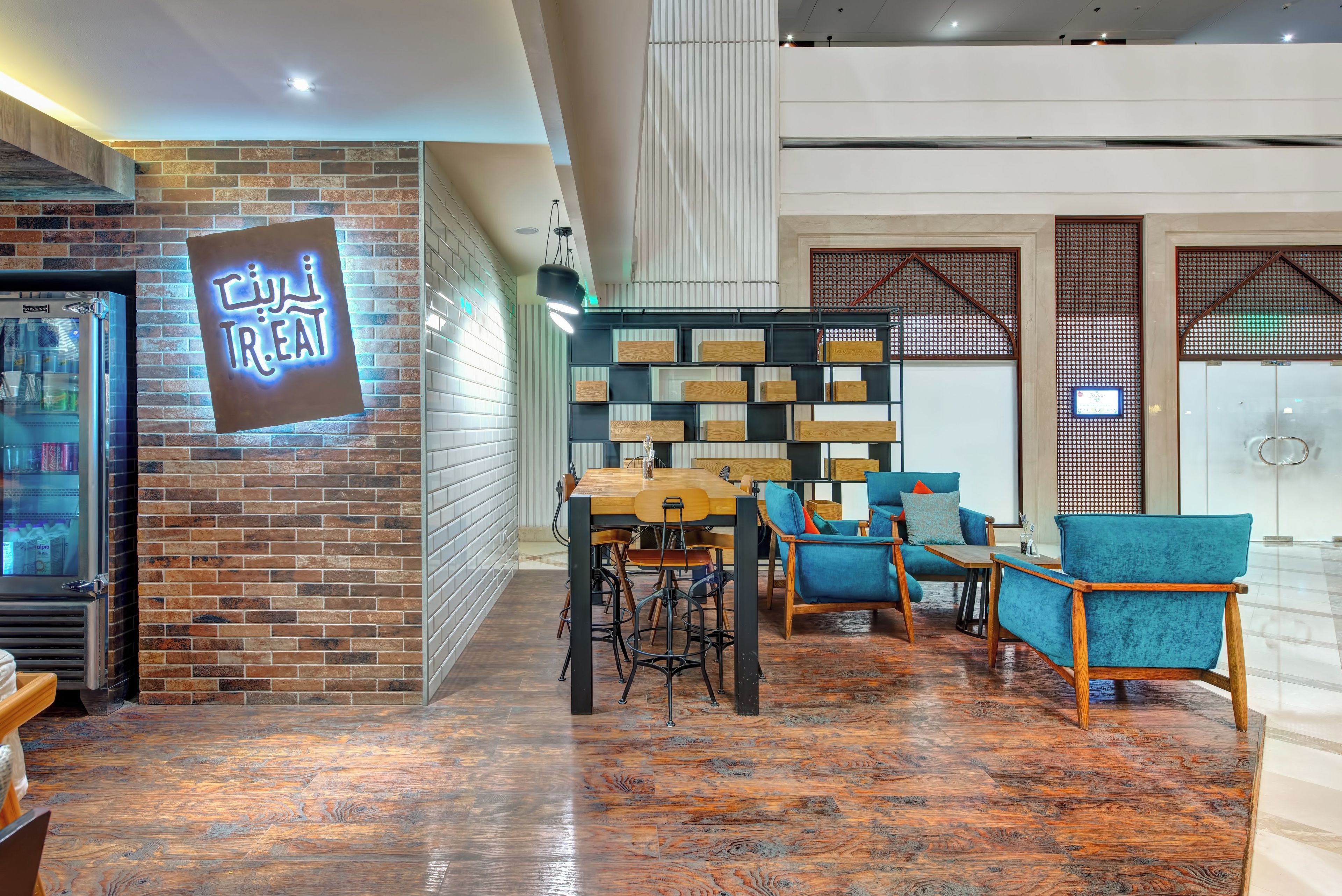 A modern interior with a brick wall, a neon sign, a wooden table, and blue chairs.