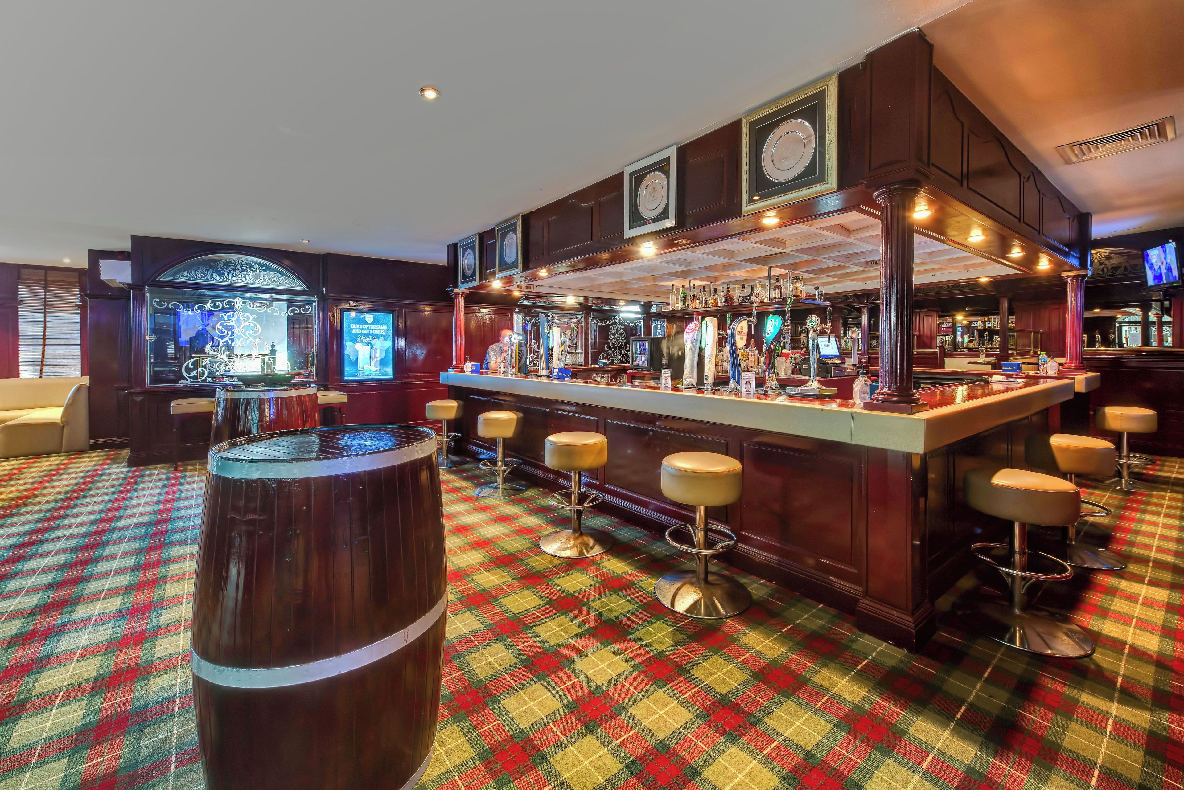 Zona de bar con taburetes, barra y un barril de madera grande.
