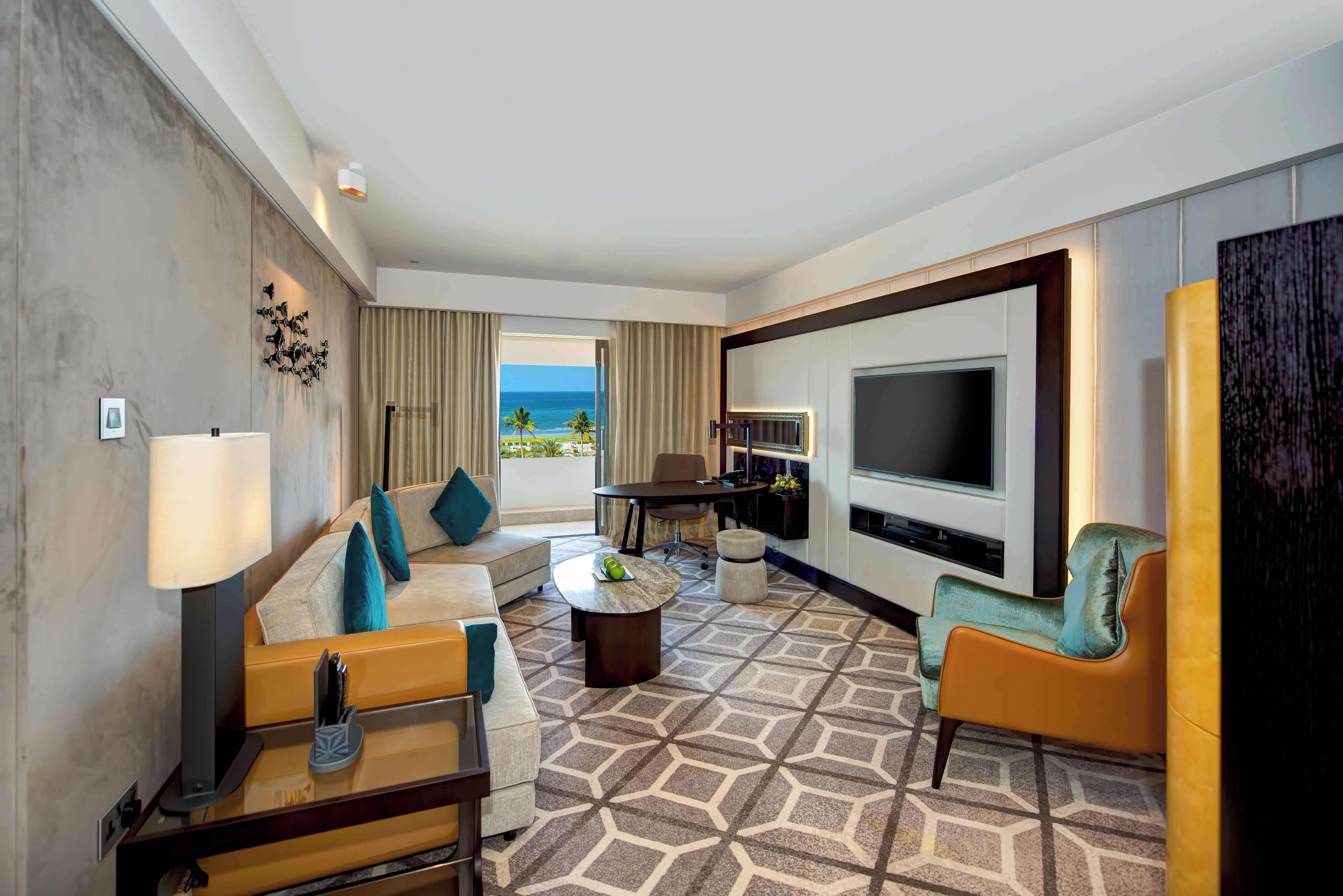 Ein Hotelzimmer mit Sofa, Sessel, Couchtisch, Fernseher und Meerblick.