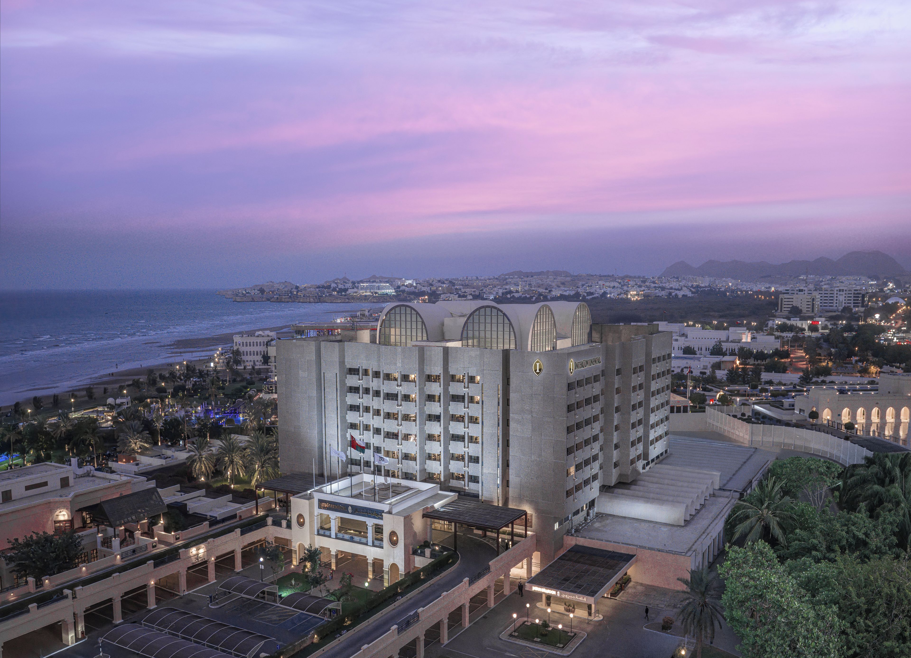 Um hotel com design arquitetônico moderno, apresentando um telhado curvo proeminente e várias varandas. O edifício está localizado perto de uma praia, oferecendo vista para o oceano.