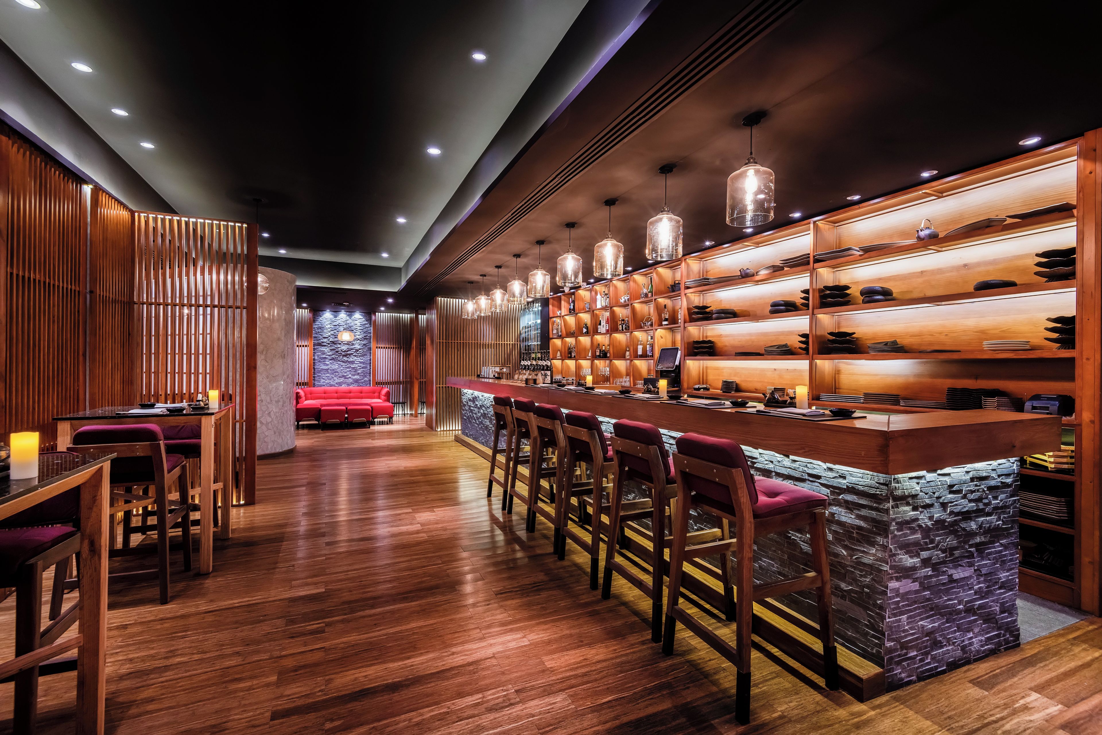 Een bar met houten planken, hangende lampen en een zithoek.