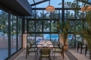 Un comedor con una mesa dispuesta para cuatro personas, rodeada de sillas, ventanas amplias y vistas a una piscina.