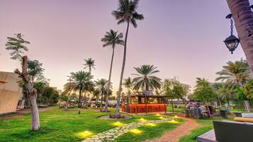 A courtyard with palm trees, a wooden gazebo, and a stone pathway.