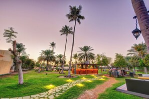 Zona de jardí amb palmeres, una glorieta i un camí.