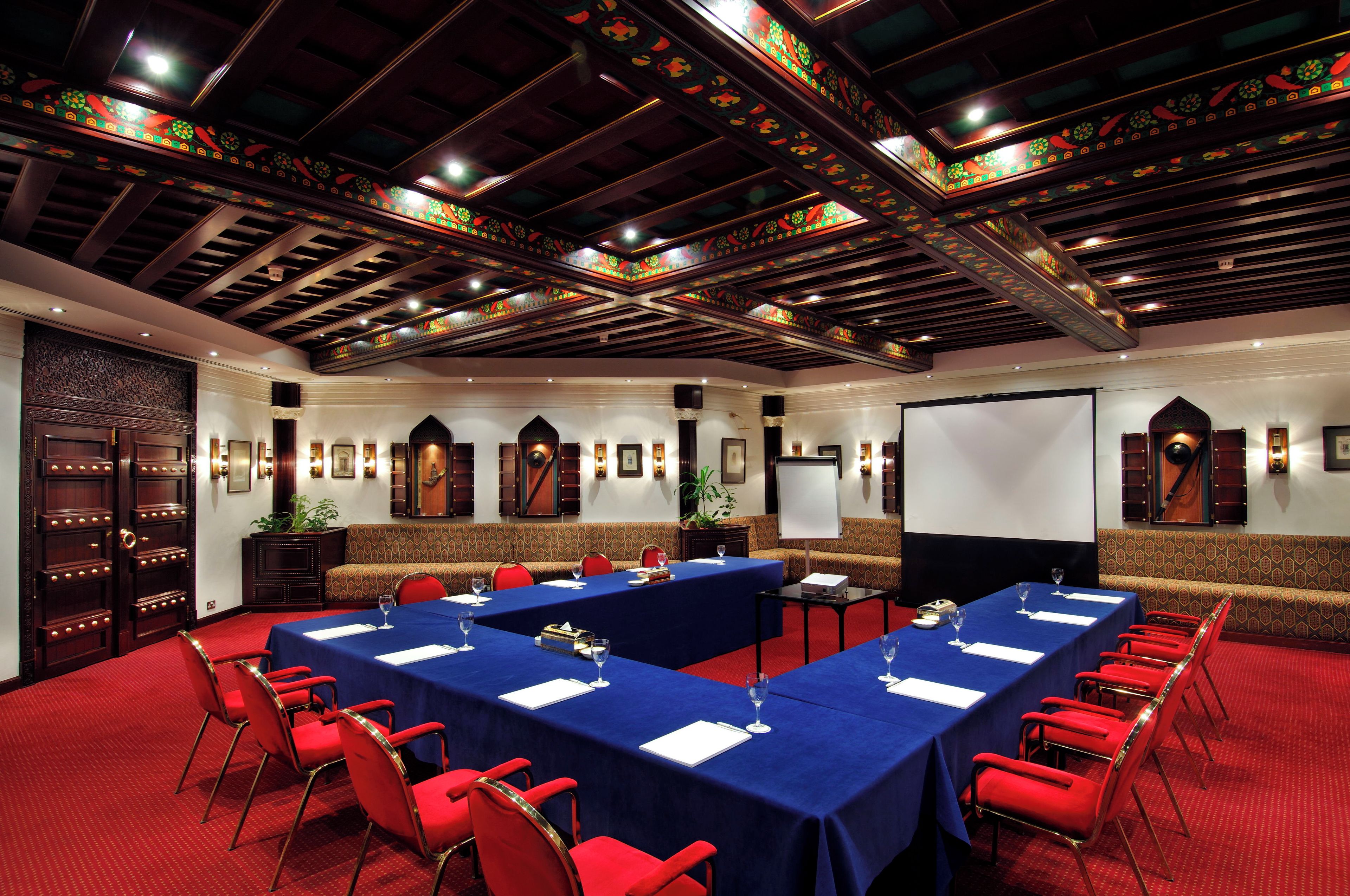 Un salón de conferencias con techo alto, paneles de madera ornamentados y una pantalla grande.