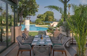 An outdoor dining area with a view of a swimming pool and palm trees.