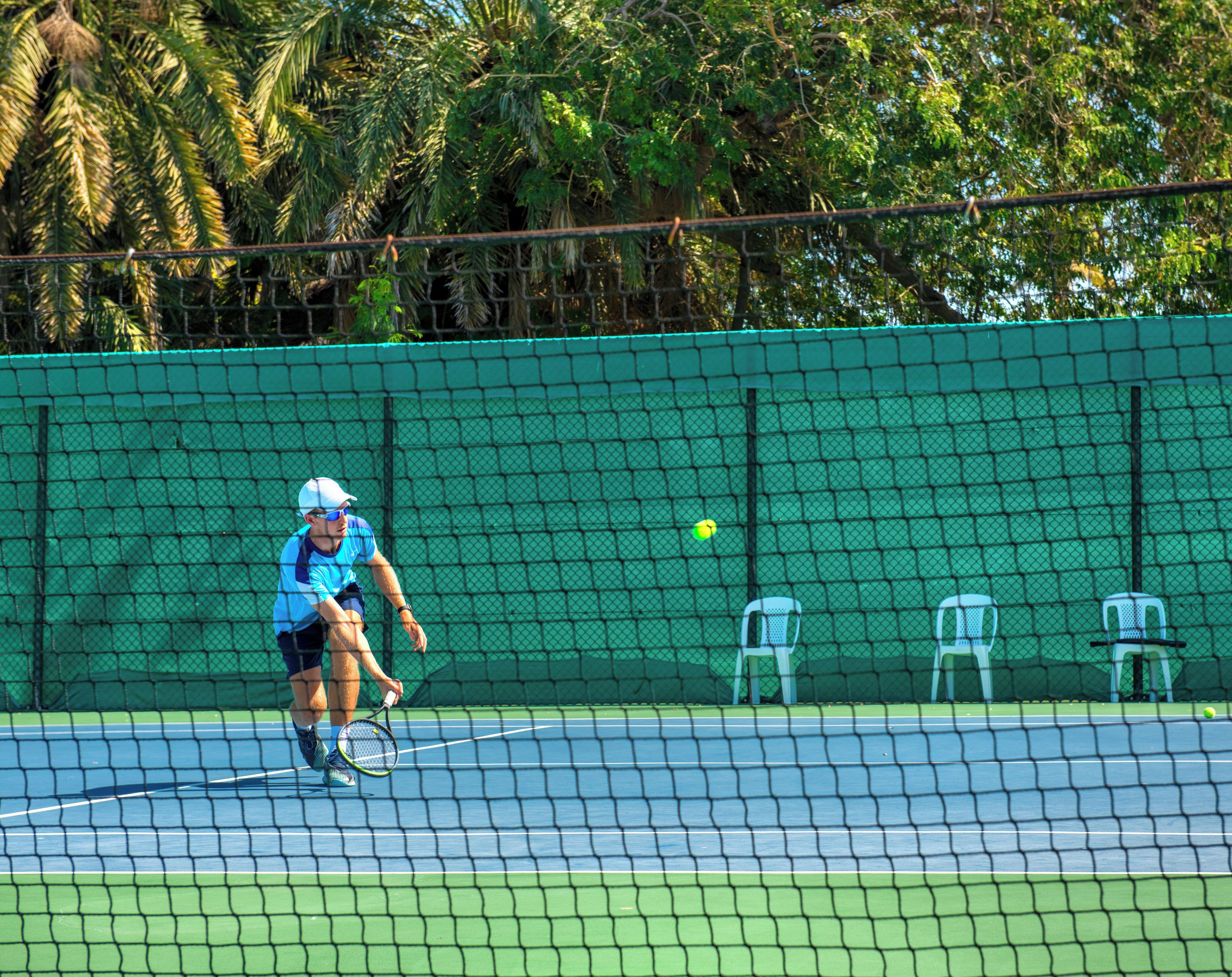 Un court de tennis avec un filet, des chaises et une clôture.