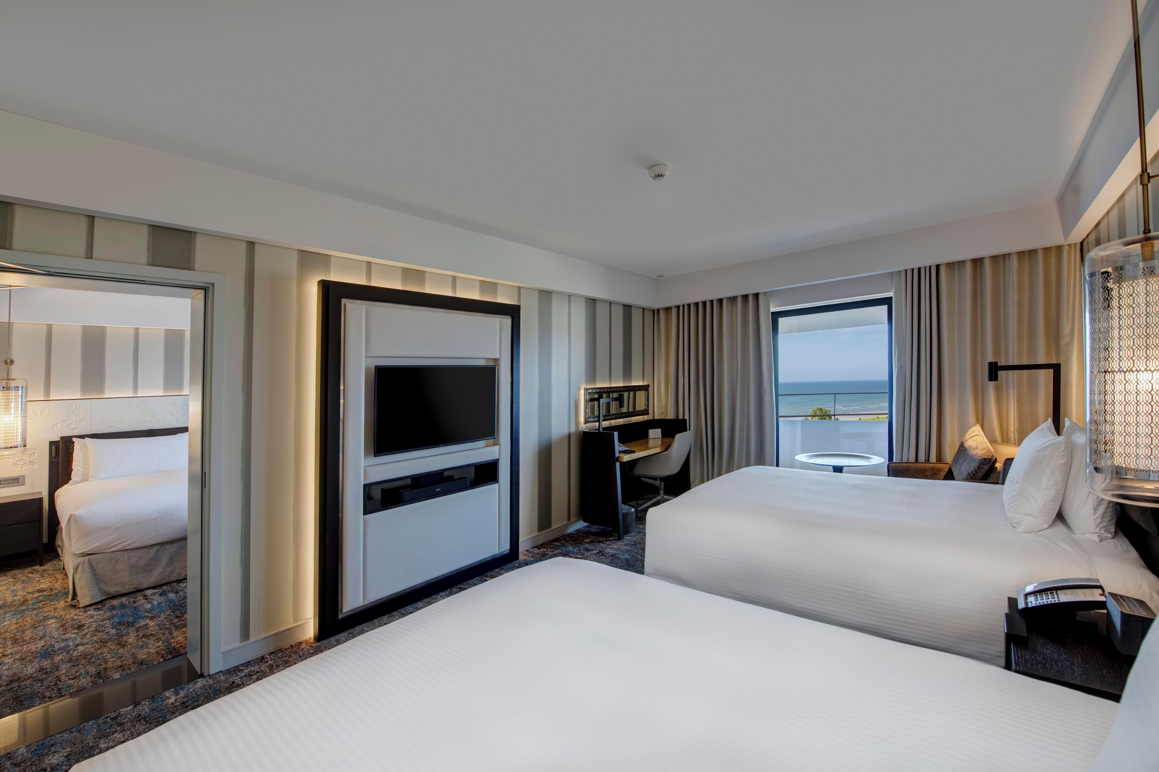 Habitación de hotel con dos camas, televisión, escritorio y vista al océano.