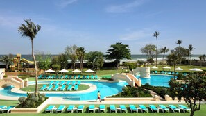 Área de piscina en un resort con múltiples tumbonas, una estructura de juegos para niños y vistas al océano.