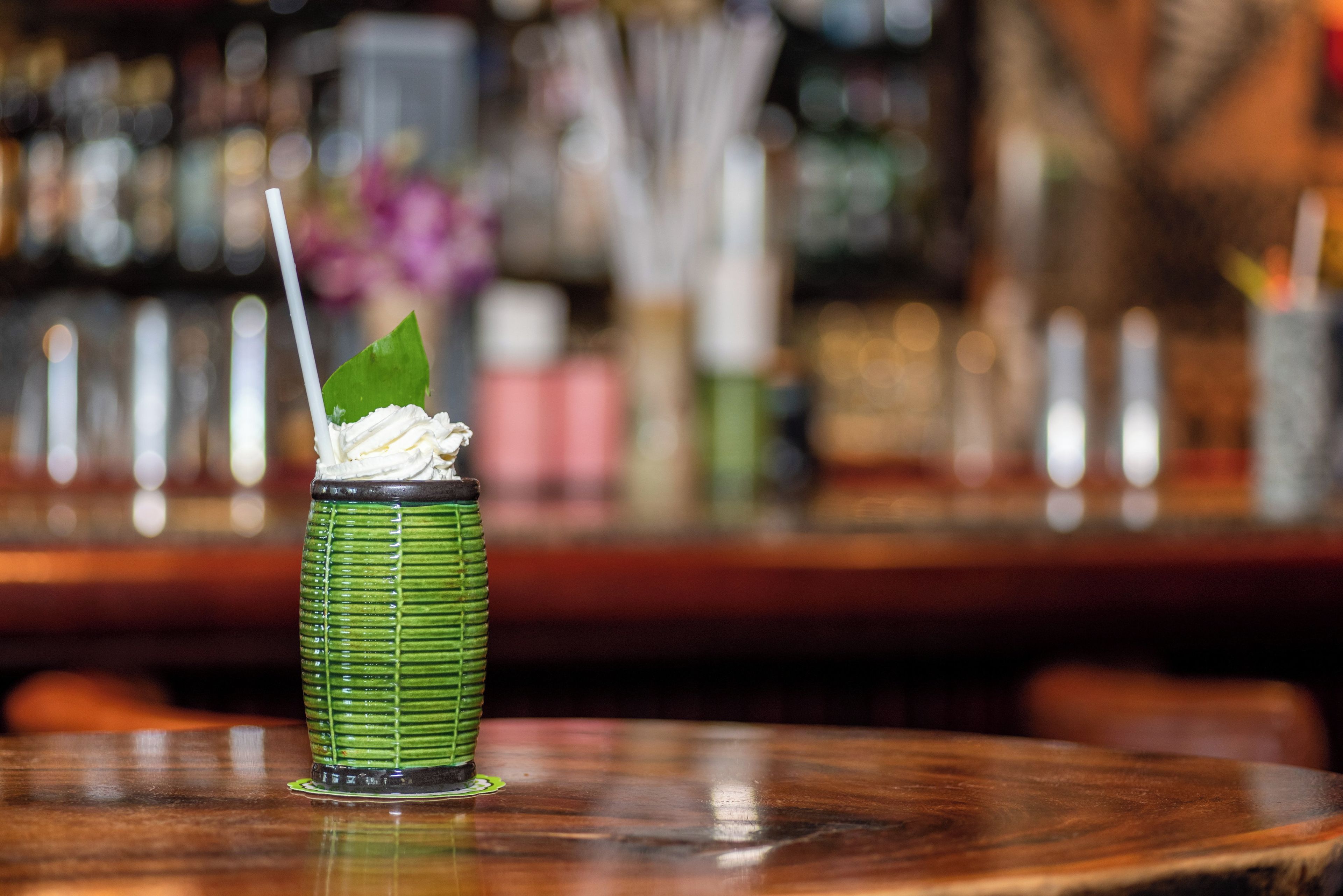 A green glass with a straw and a leaf garnish on a bar counter.