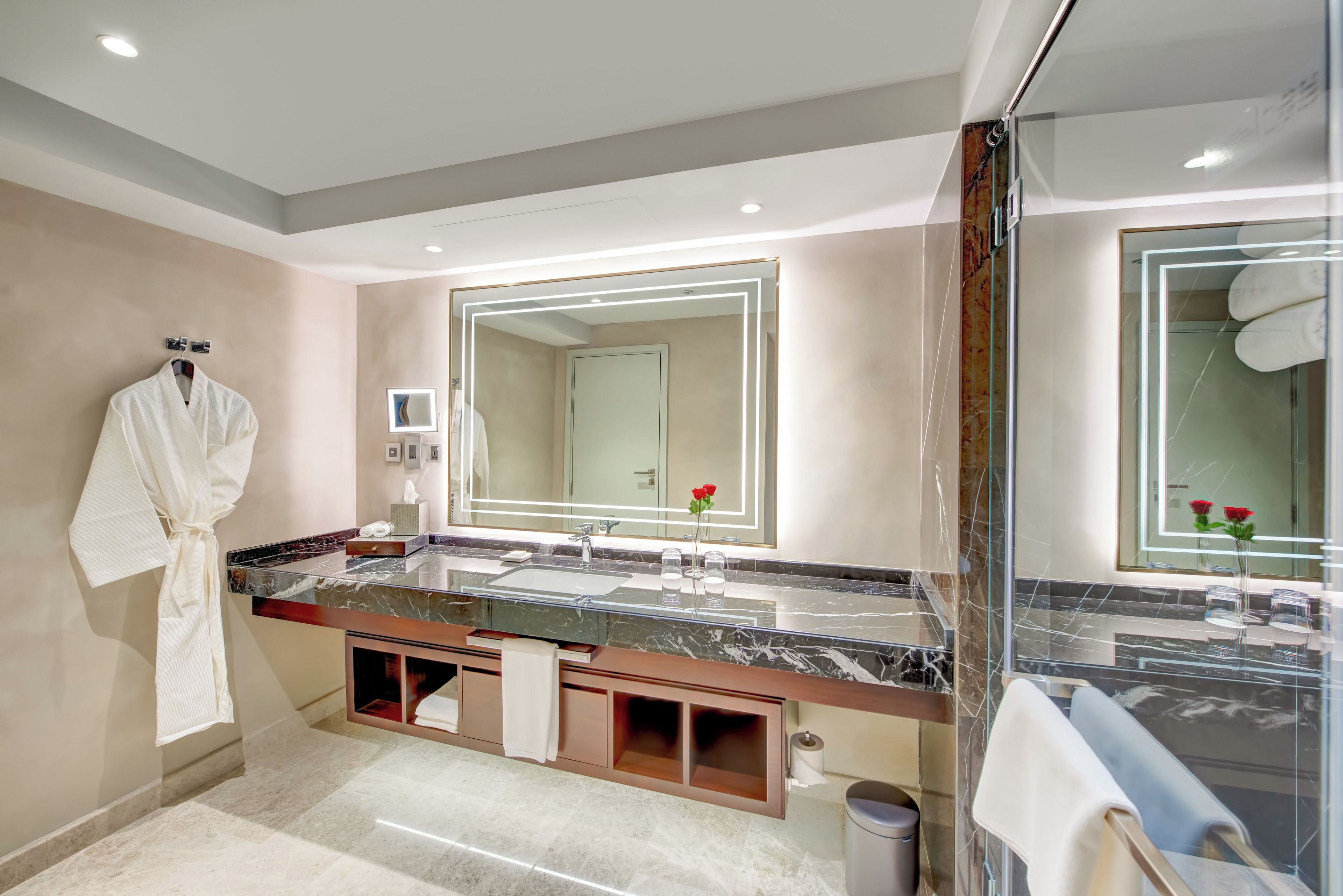 Une salle de bain moderne avec un grand miroir, un comptoir en marbre et un peignoir accroché au mur.