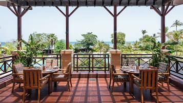 A terrace with wooden furniture, a pool, and a view of the ocean.