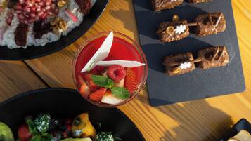 Variedad de alimentos sobre una mesa, incluyendo un bol de ensalada de frutas, un plato de arroz con nueces y semillas de granada, y dulces cubiertos de chocolate.