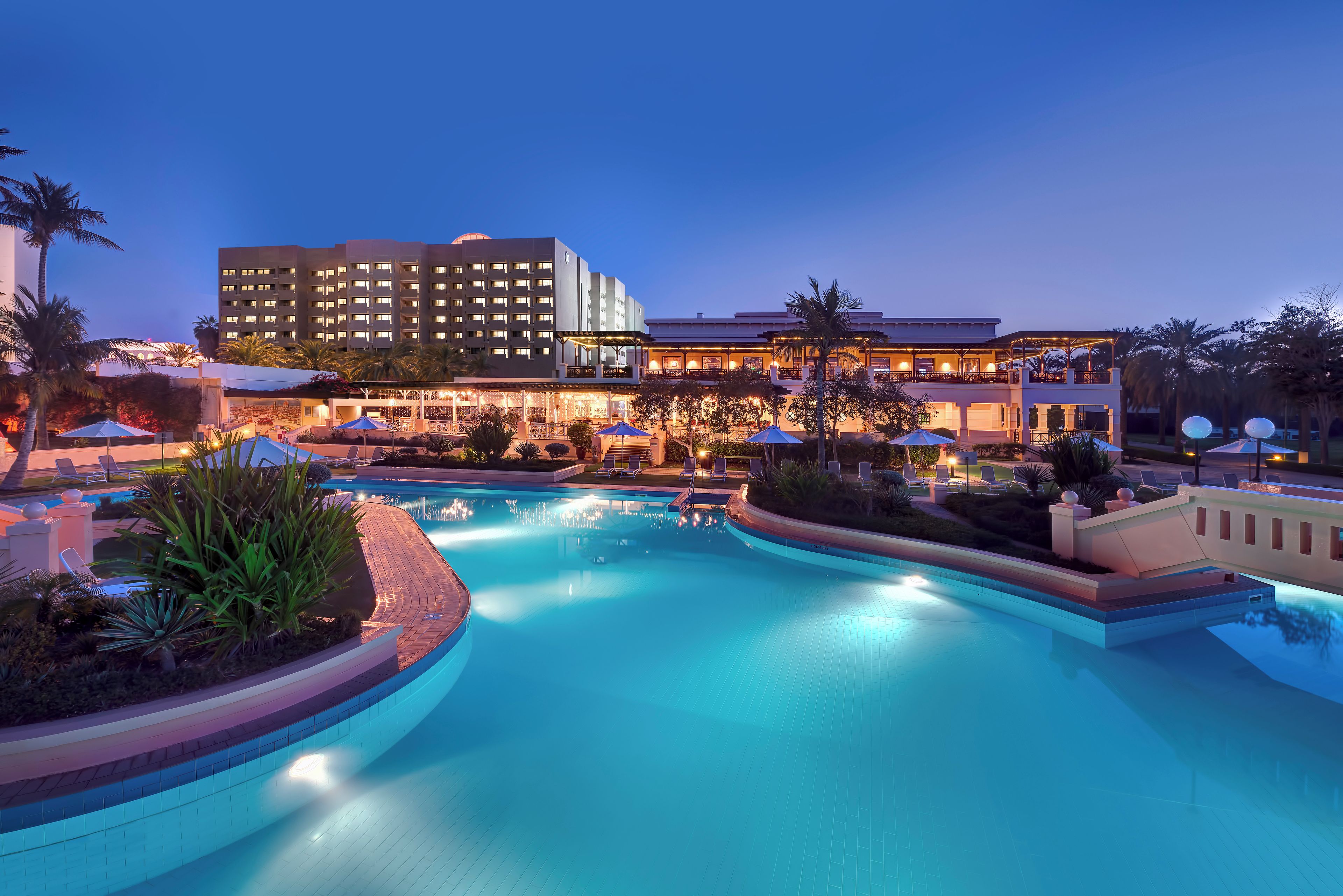 A hotel with a swimming pool, outdoor seating, and palm trees.