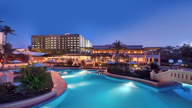 A hotel with a swimming pool, outdoor seating, and palm trees.