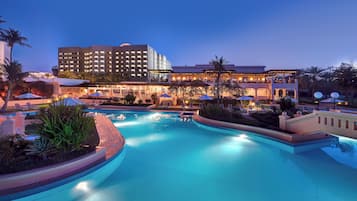 A hotel with a swimming pool, outdoor seating, and palm trees.