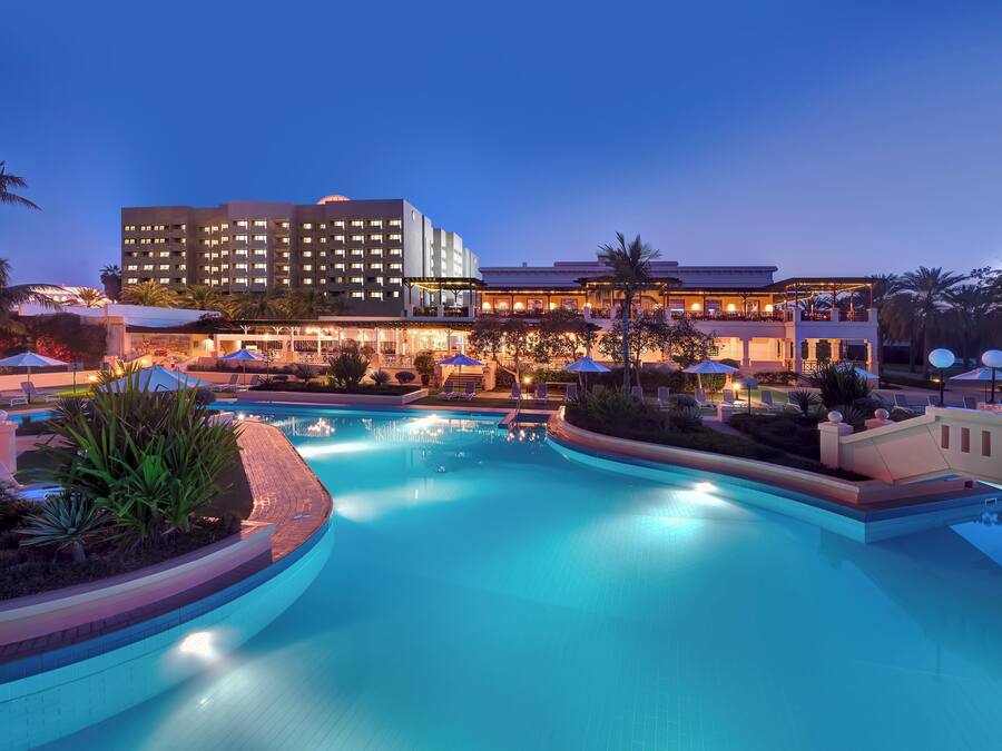 A hotel with a swimming pool, outdoor seating, and palm trees.