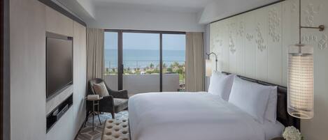 Une chambre d’hôtel avec un grand lit, une télévision, une chaise, une petite table et une vue sur l’océan.