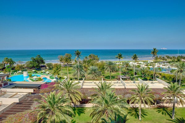 A resort with a swimming pool, palm trees, and a view of the ocean.