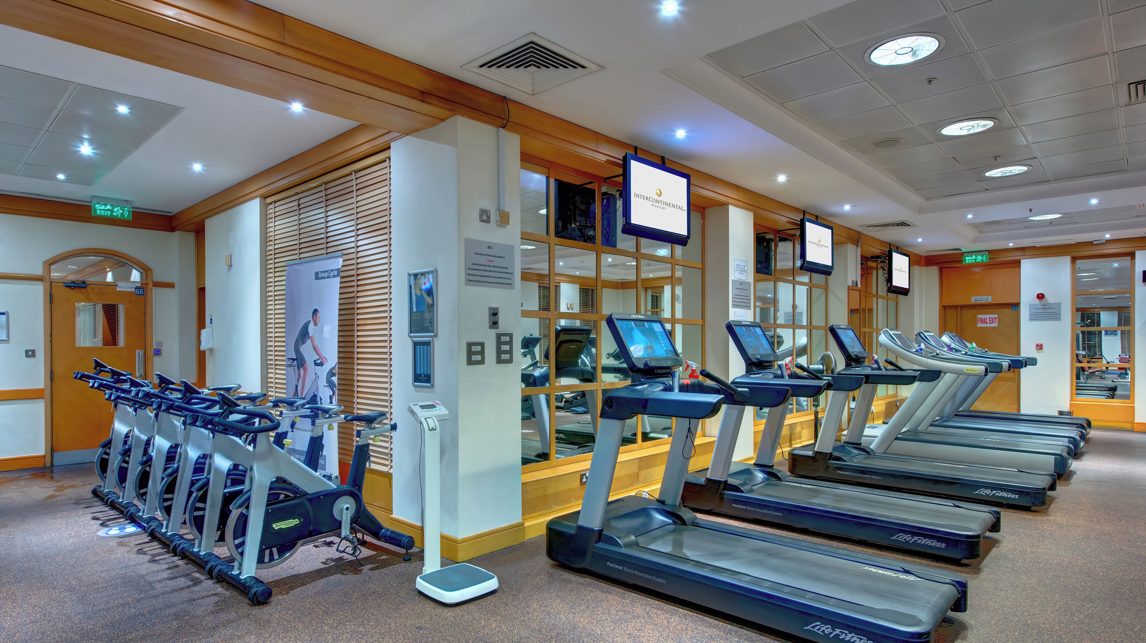 Un gimnasio con cintas de correr, bicicletas estáticas y un espejo grande.