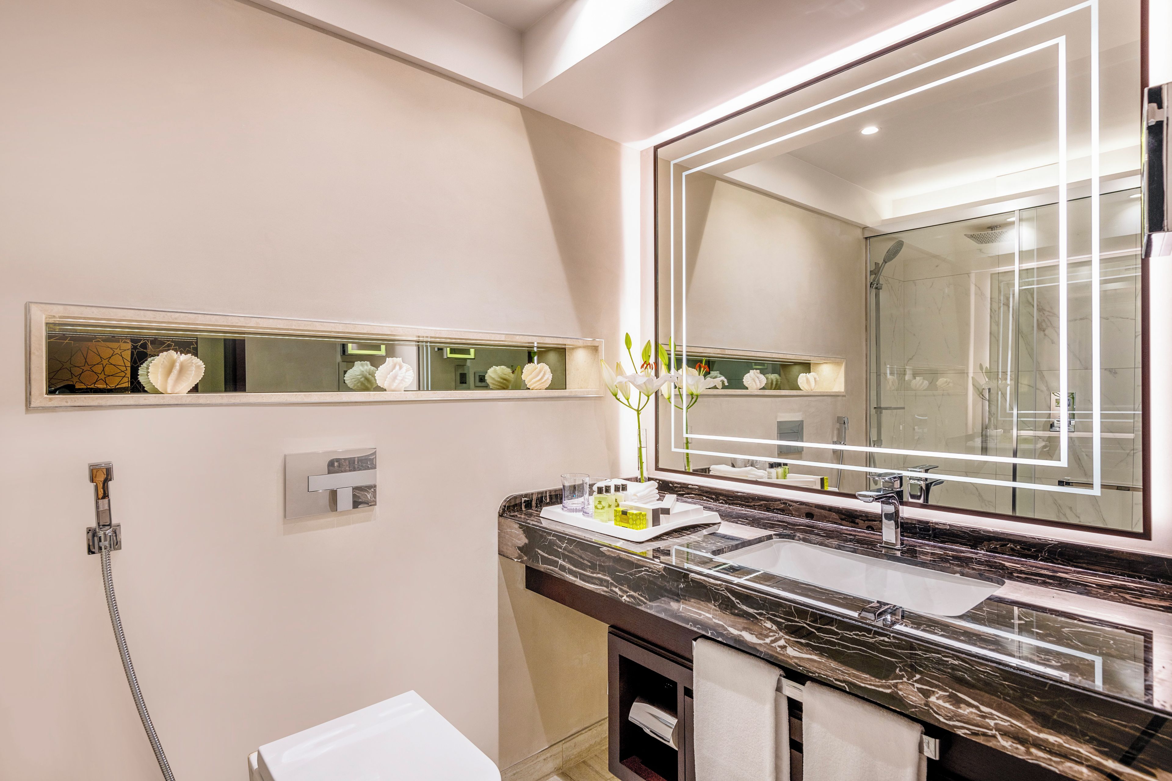 A modern bathroom with a large mirror, a marble countertop, a glass-enclosed shower, and a towel rack.