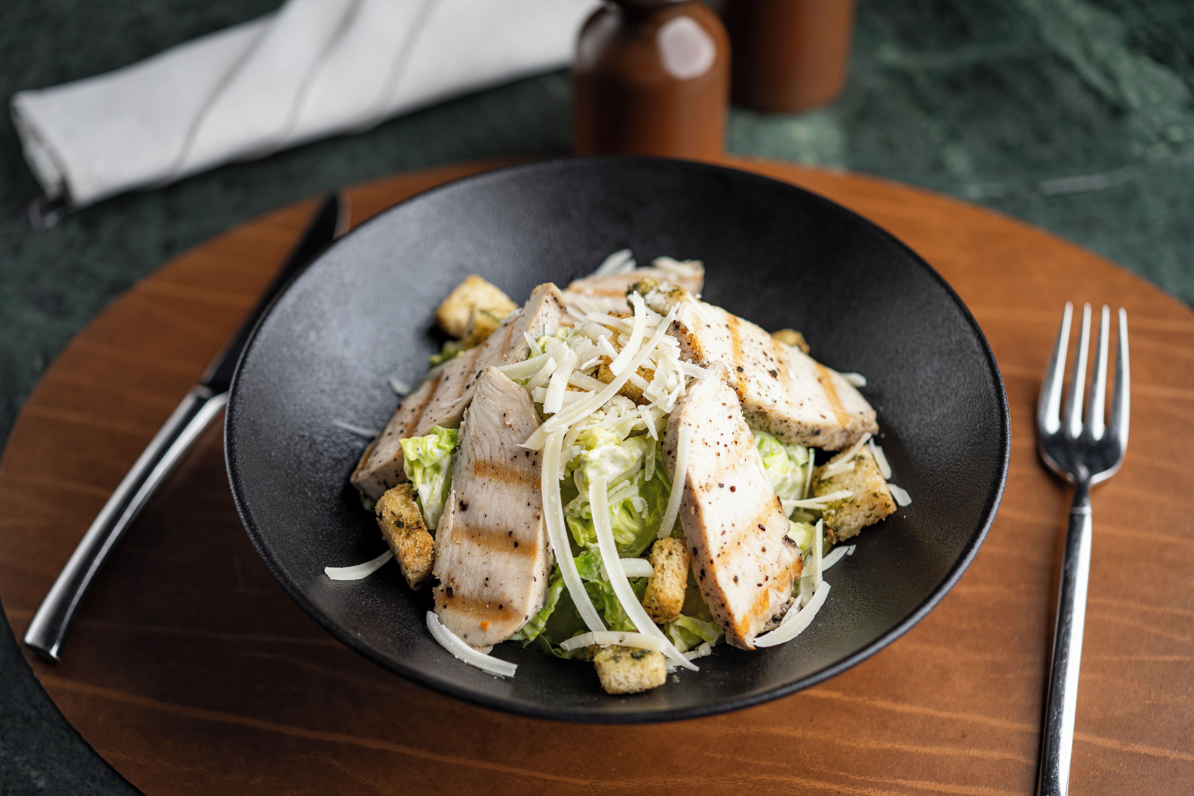 Un plato de comida con pollo, lechuga y croutons sobre un plato oscuro.